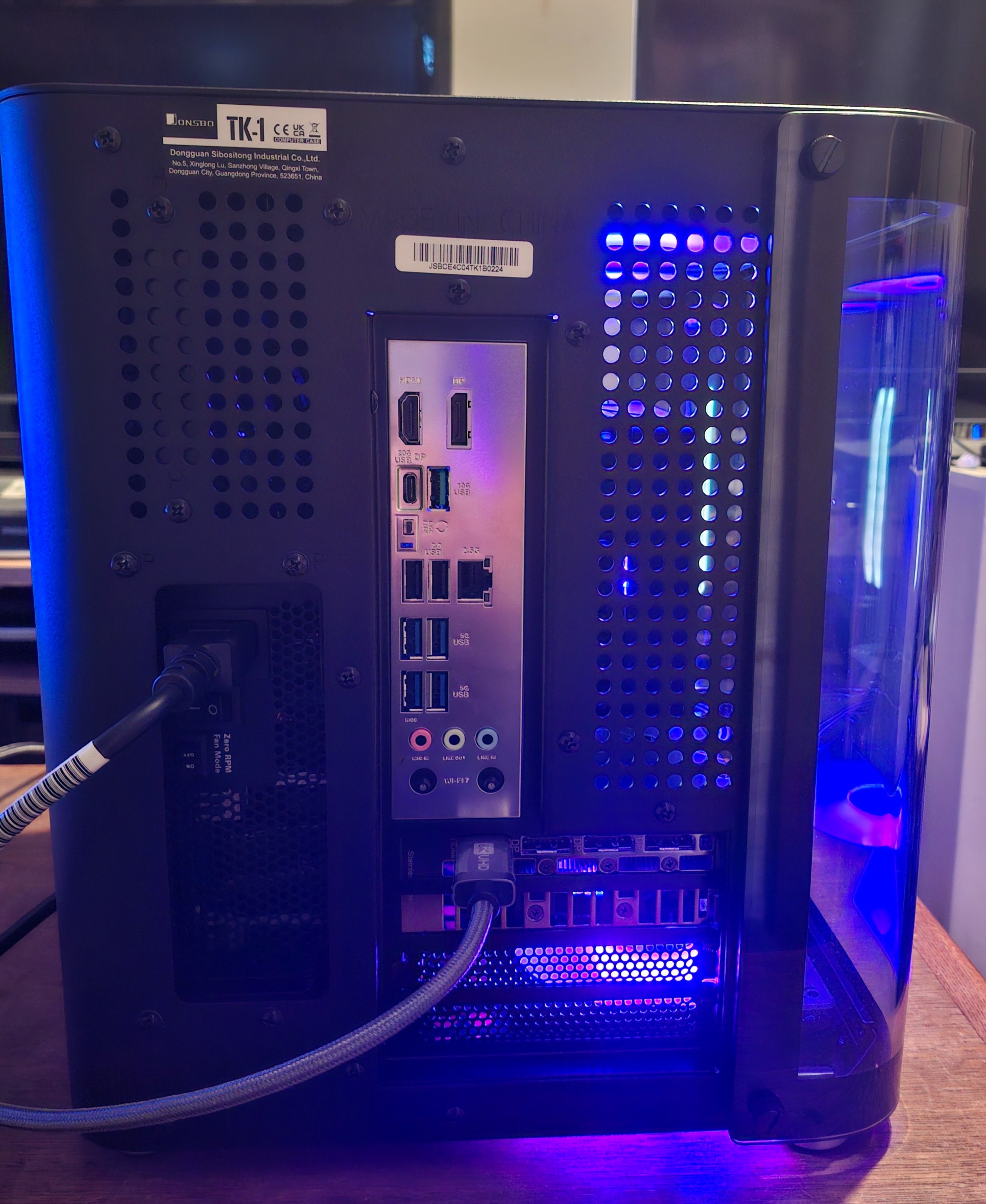 Rear view of a desktop PC tower with blue LED lighting, showing the I/O panel with USB and video ports and perforated ventilation.